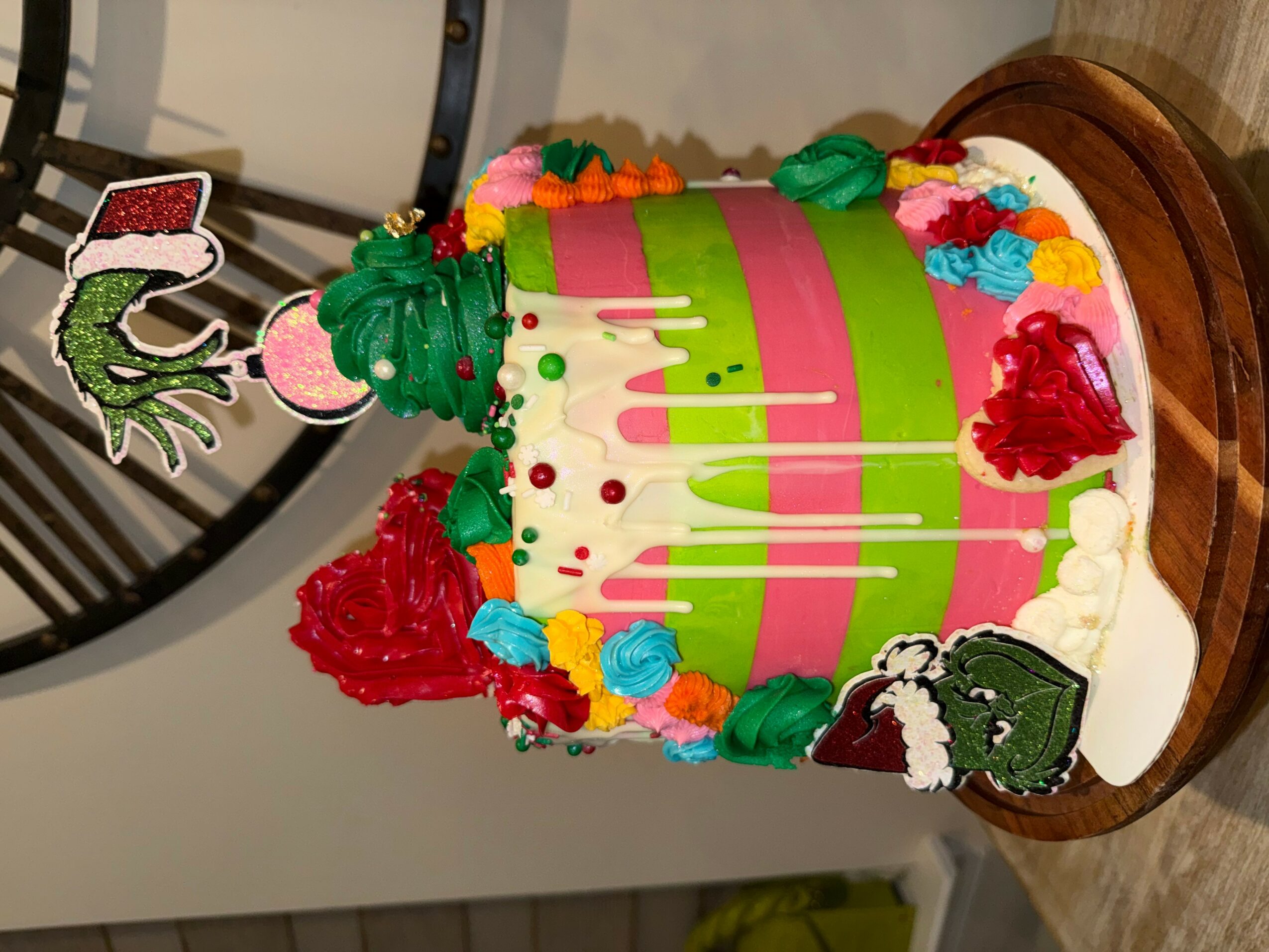 Colorful birthday cake with pink, green, and white stripes, decorated with flowers, a Santa figure, and a small gift box.