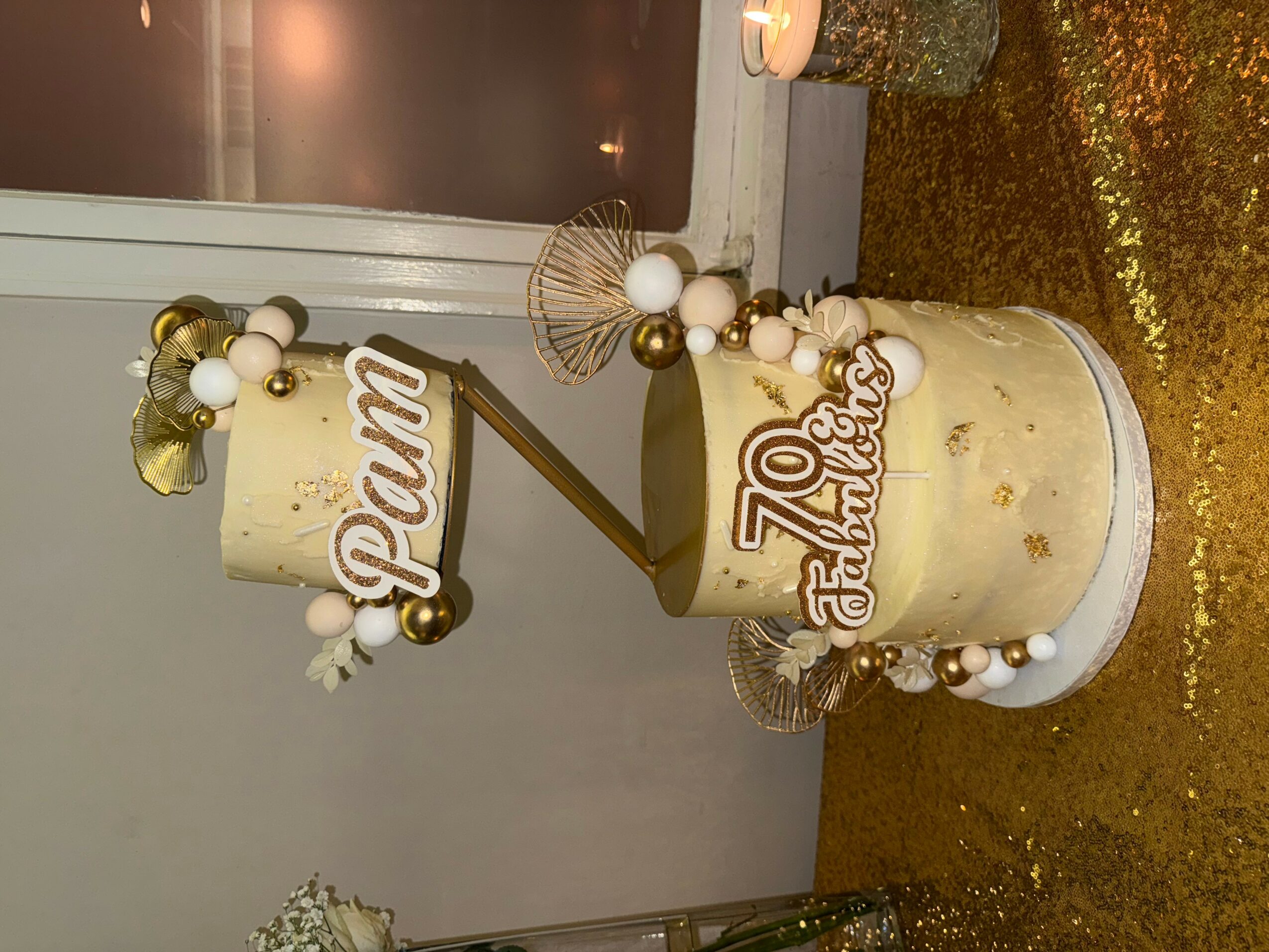 Celebration cake with gold and white decorations, including a sign that says '70 Fabulous' and a 'Dream' topper.