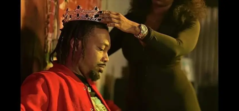 Person wearing a crown is being crowned by another person, with a blurred background.