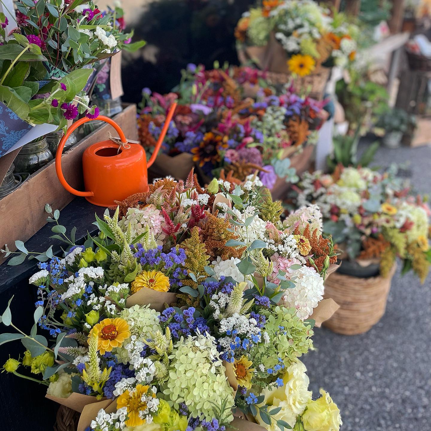 Colorful assortment of fresh flowers including sunflowers, hydrangeas, and daisies displayed at a market stall.