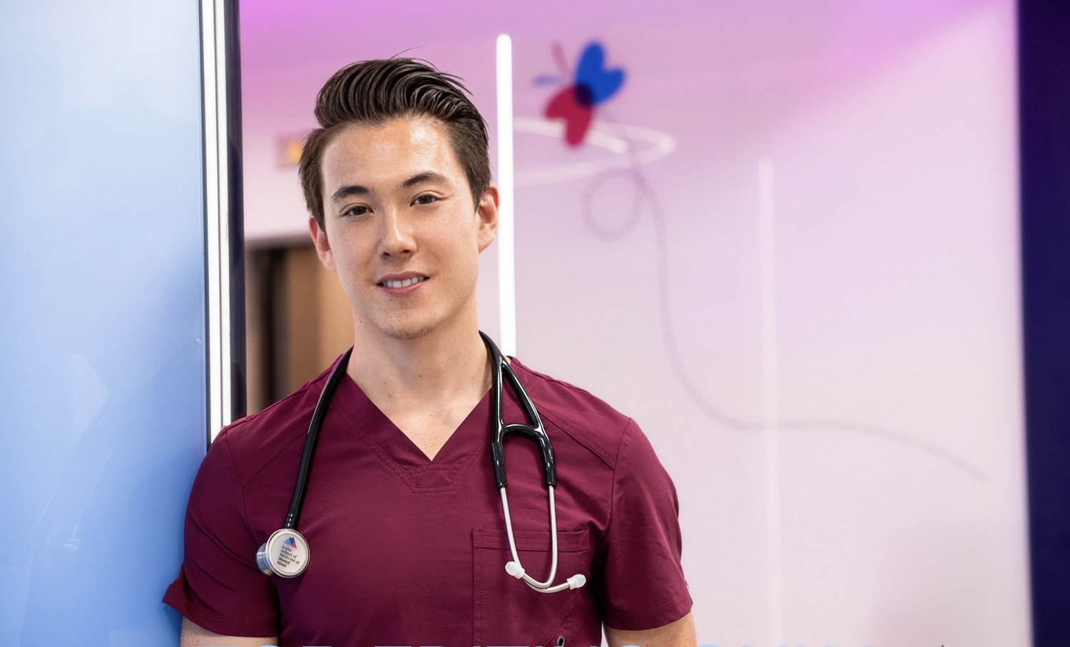 Young healthcare professional with stethoscope standing in a colorful medical setting.