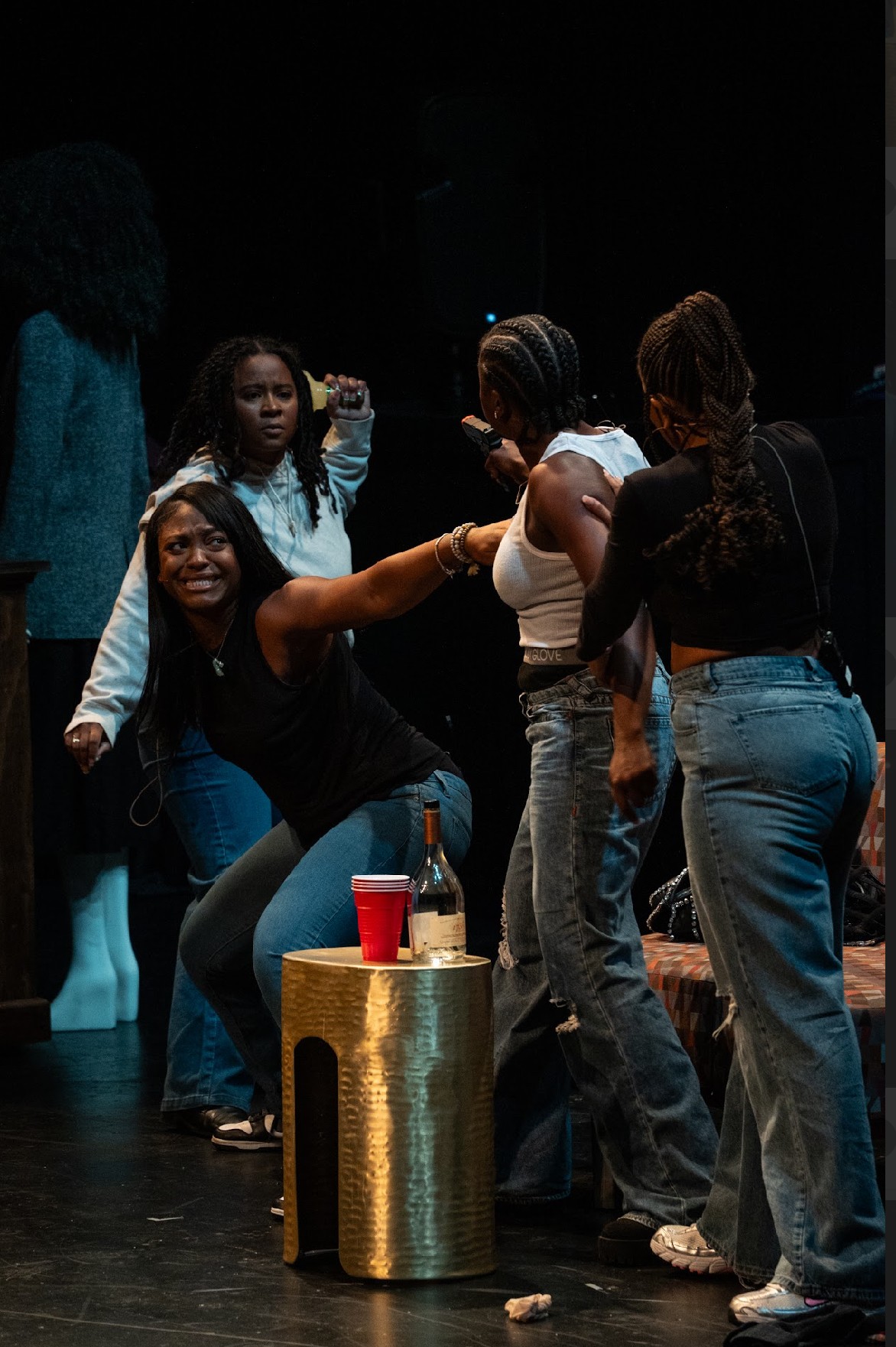 Group of women on stage, some smiling and talking, with a gold cylindrical object and red cup in foreground.
