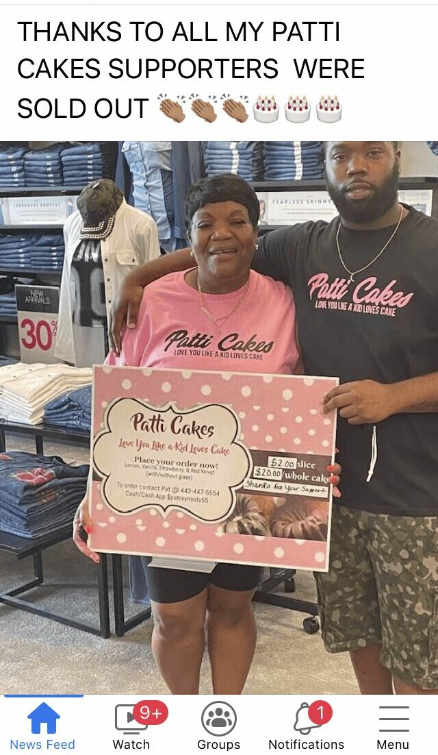 Two people holding a cake box, smiling, in a store with shelves and a person in the background.