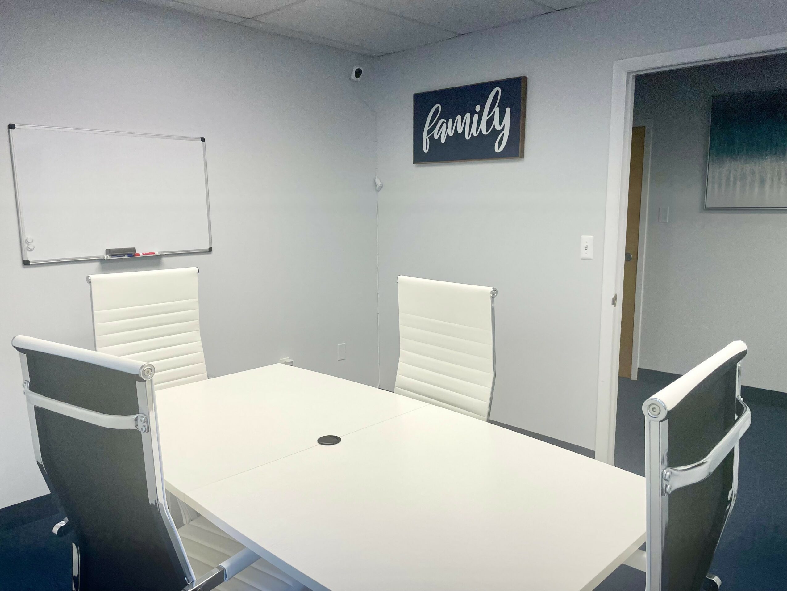Meeting room with white table, four chairs, whiteboard, and a wall sign reading 'family'.
