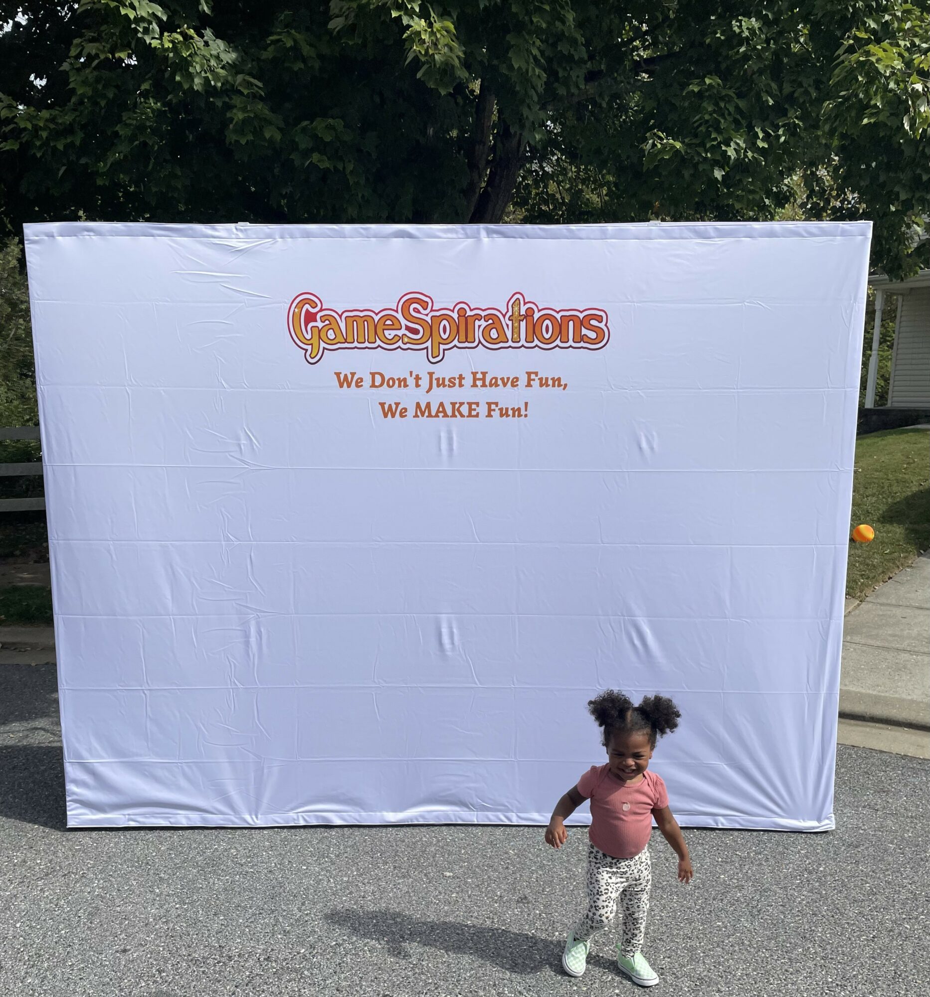 Young girl standing in front of a large white backdrop with colorful text, outdoors on a sunny day.