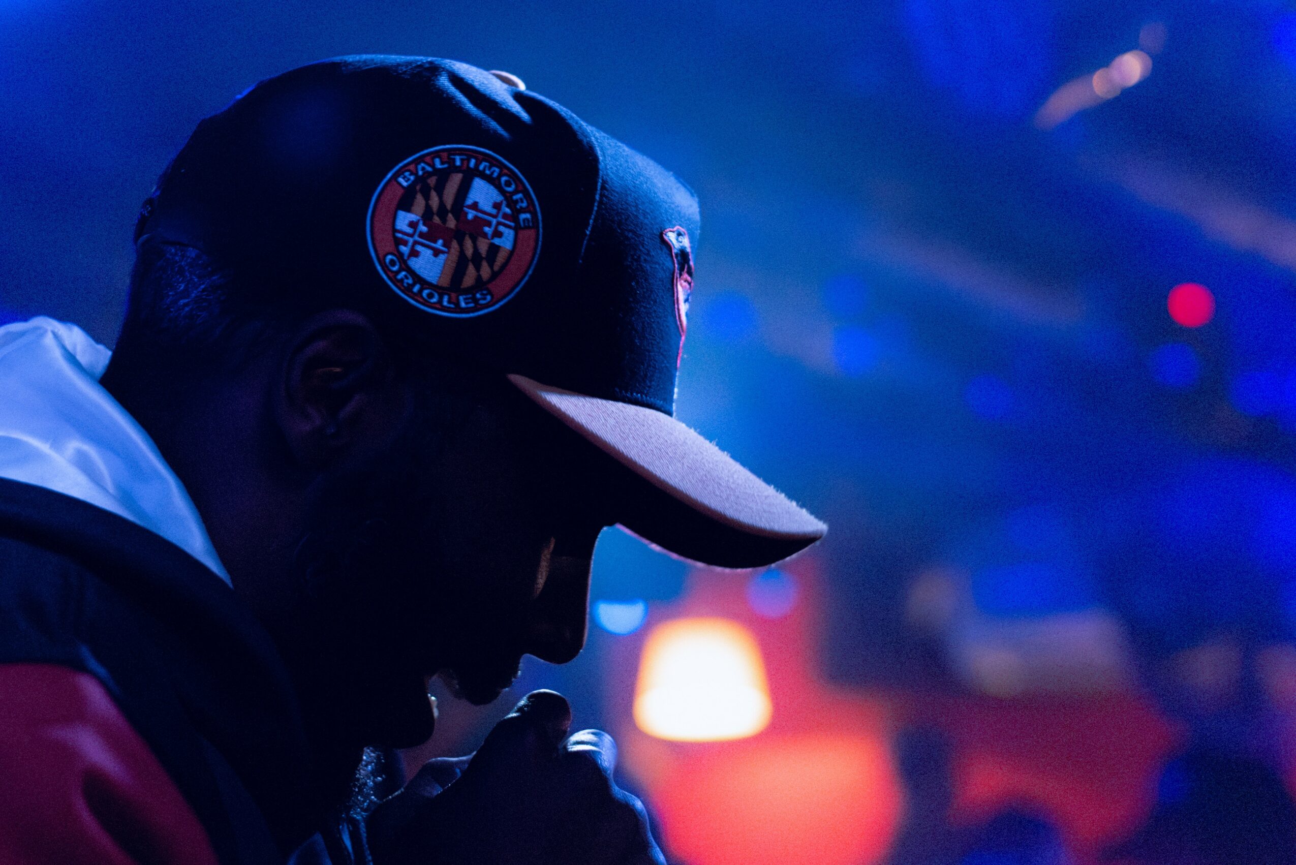 Silhouette of a person wearing a cap with a logo, in a dimly lit environment with blue and red lighting.