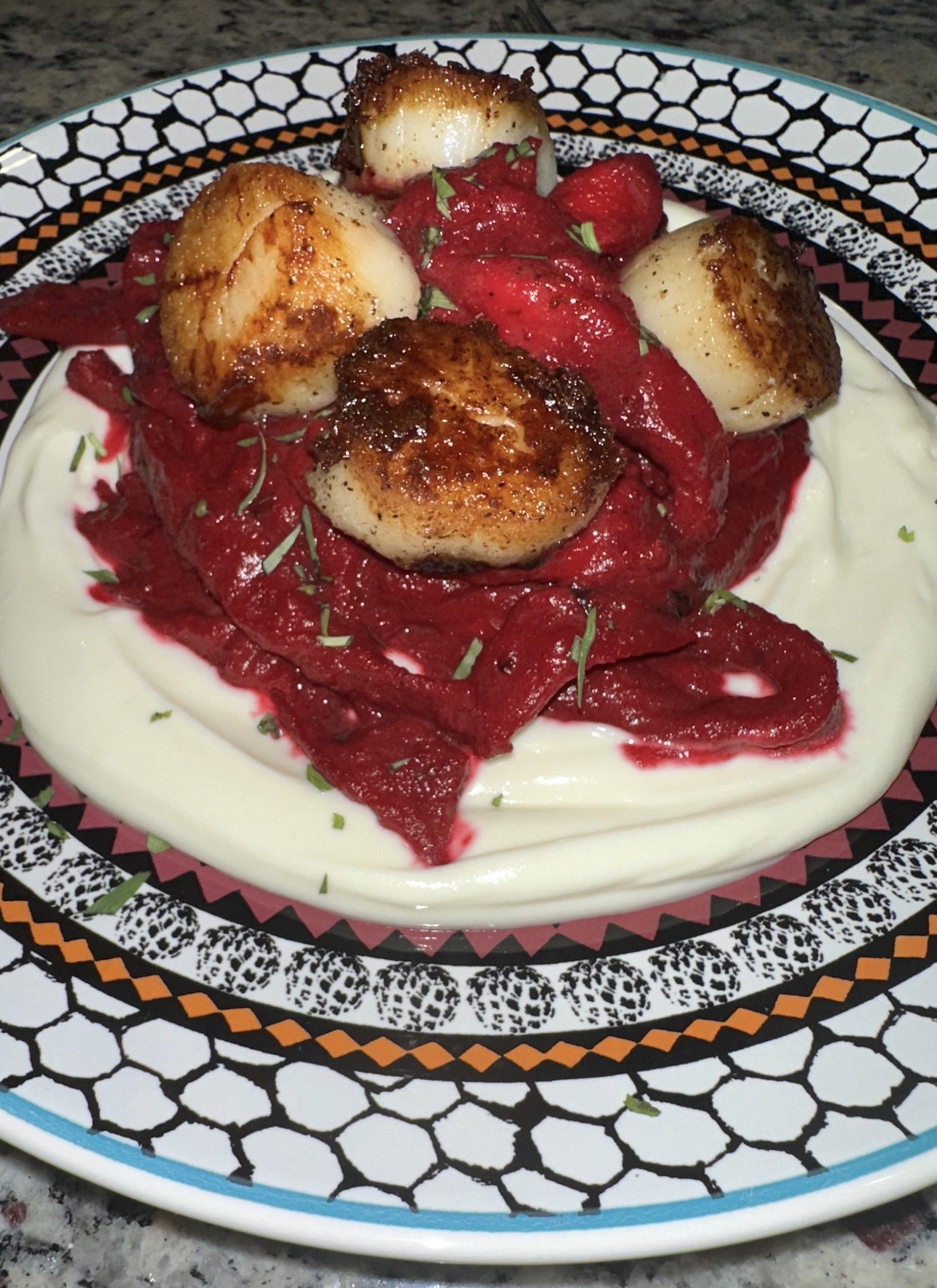 Plate with seared scallops, red beetroot, and white sauce, on a patterned black and white dish.