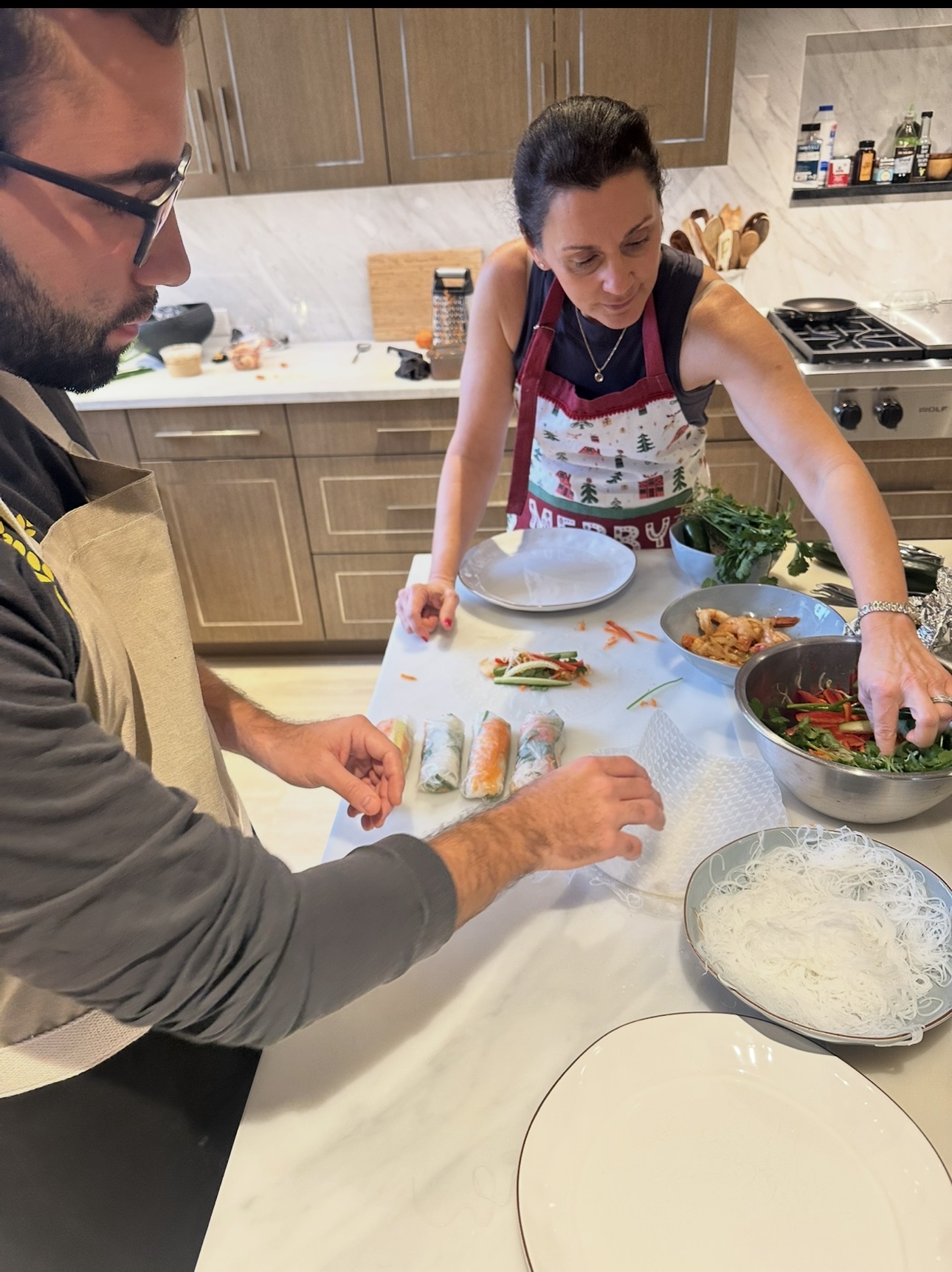 Two people preparing sushi in a kitchen, with ingredients and plates on the counter.