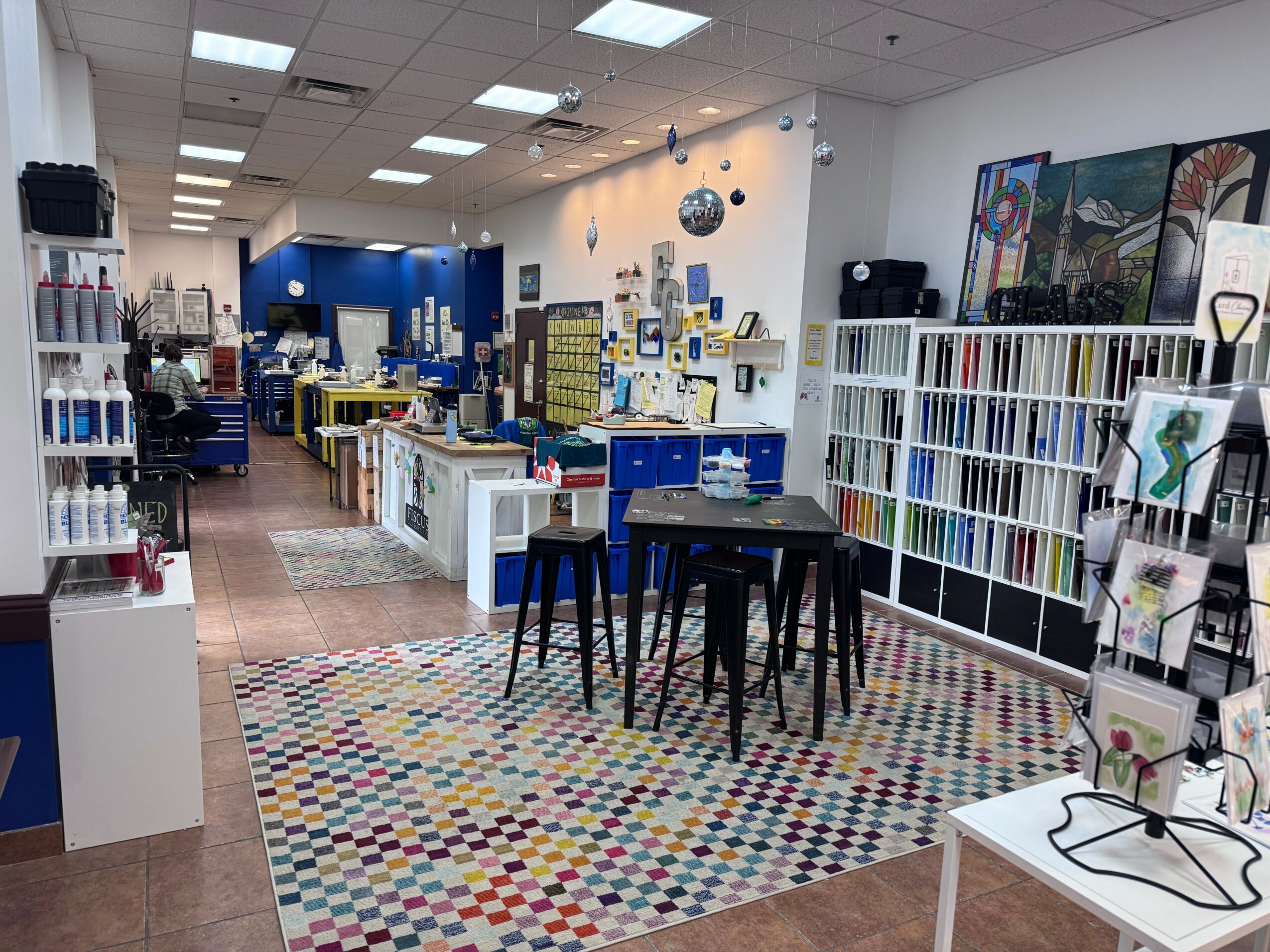 Interior of a store with shelves, tables, and colorful patterned floor, displaying books, stationery, and art supplies.