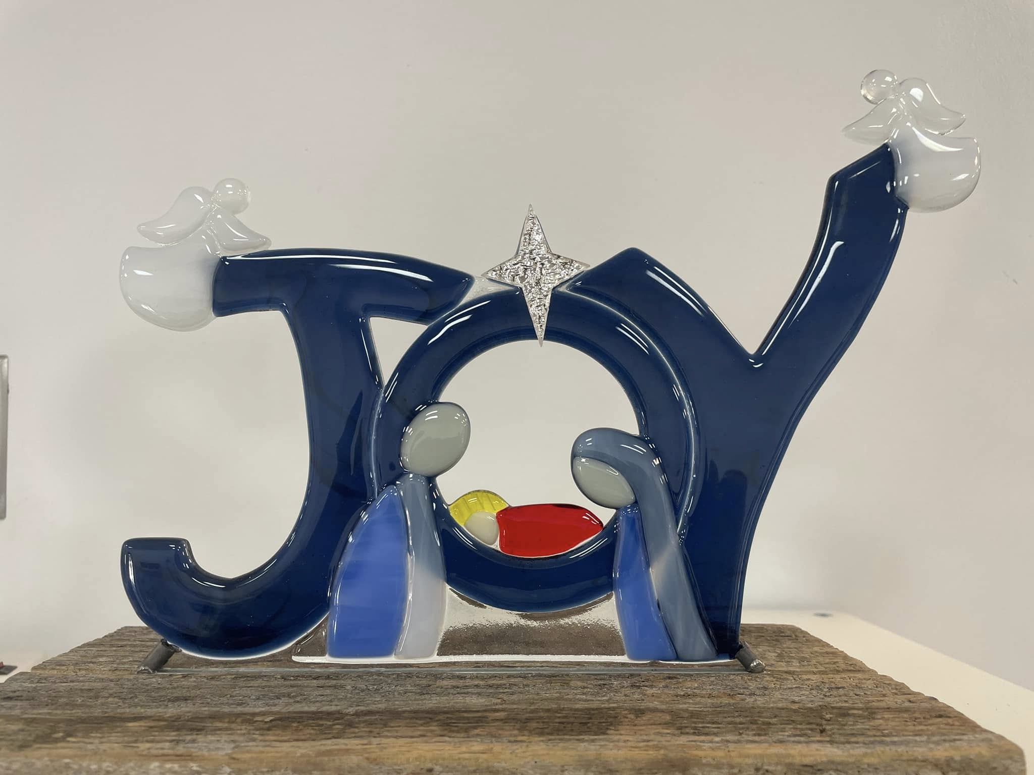 Glass sculpture spelling 'Joy' with a star, water droplets, and a rainbow-colored element, on a wooden surface.