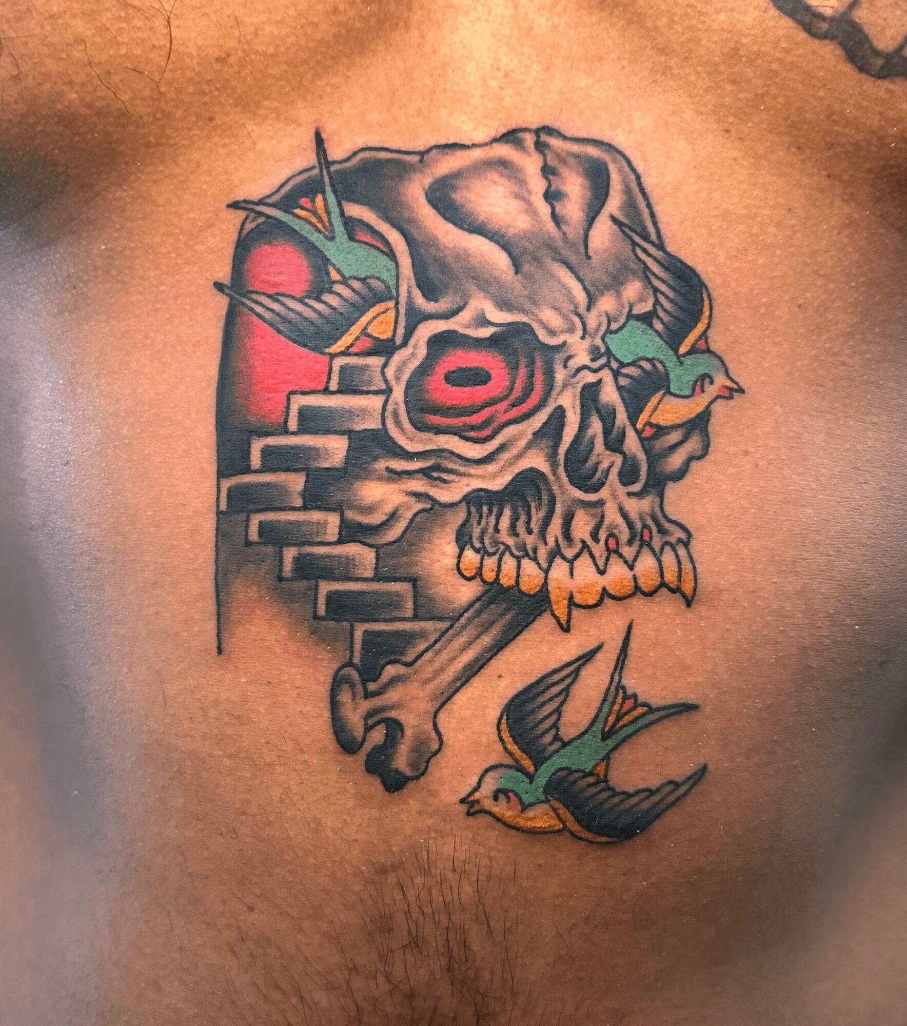 Tattoo of a skull with stairs, a sword, and two birds, in a colorful, traditional style.