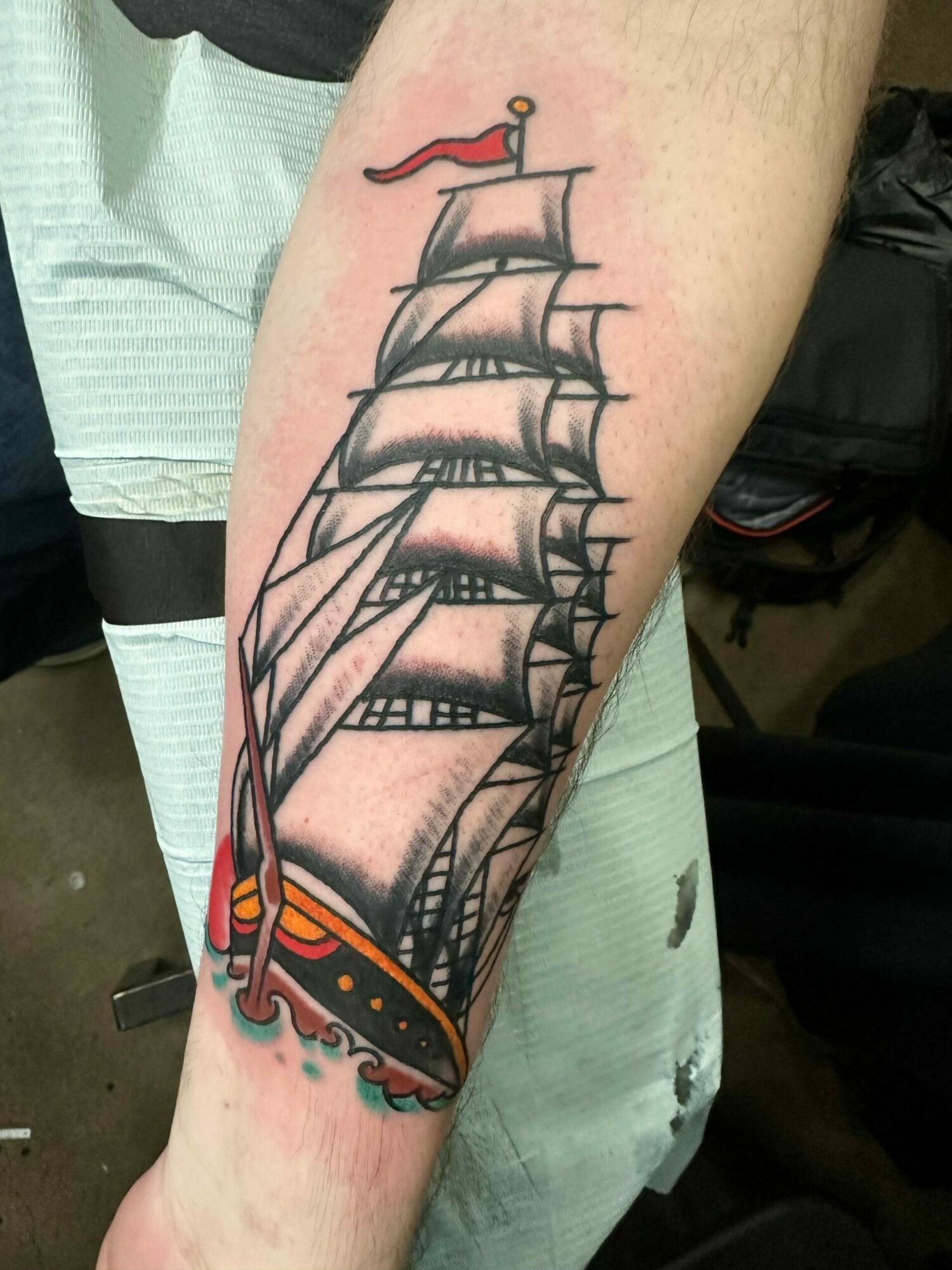 Tattoo of a sailing ship with sails, rigging, and a decorative hull on person's forearm.