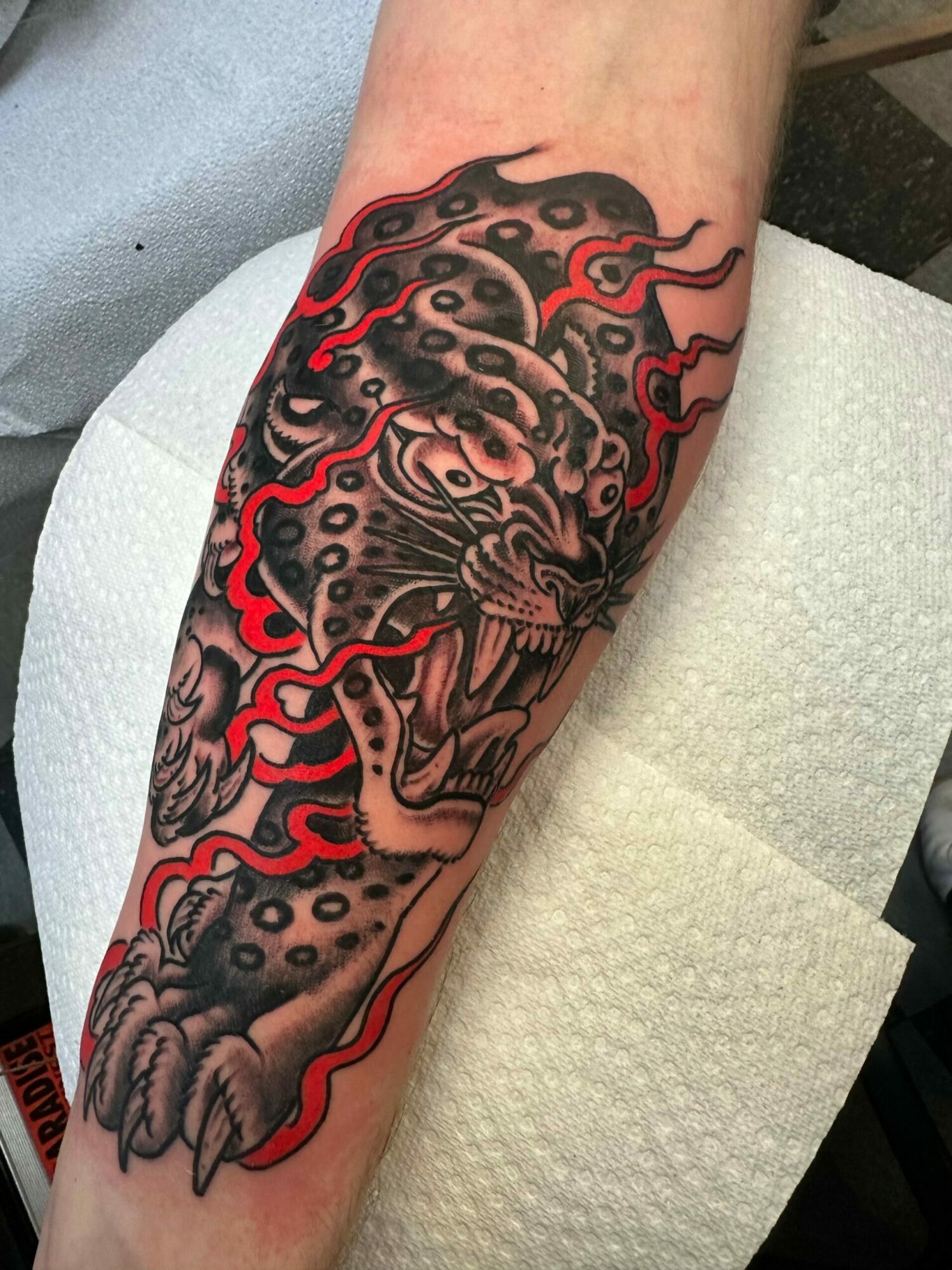Tattoo of a dragon with flames, detailed scales, and claws on person's arm.