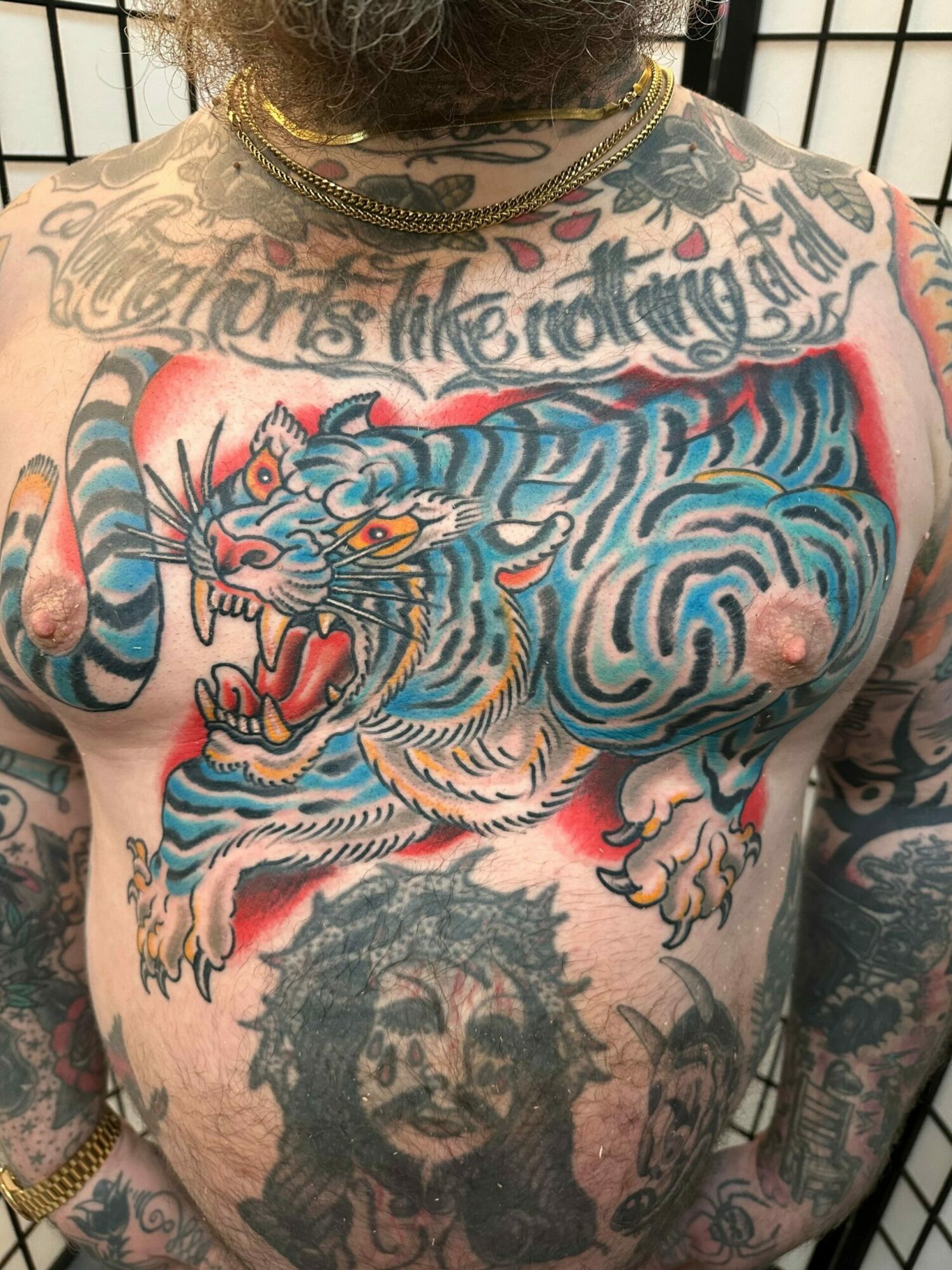 Close-up of a person's chest and shoulder tattoos, including a blue tiger with orange eyes and other designs.
