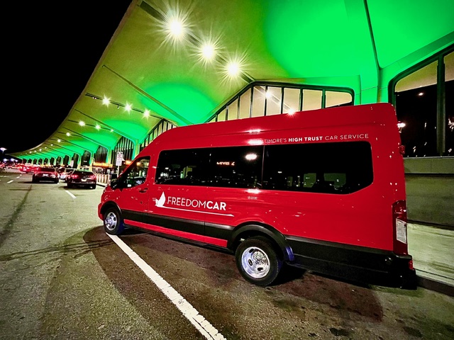 Red van with 'FREEDOMCAR' logo parked outside a modern building illuminated with green and white lights at night.