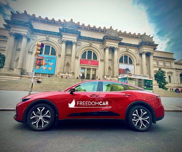 Red car with 'FREEDOMCAR' logo parked in front of a historic building with columns and arched windows.