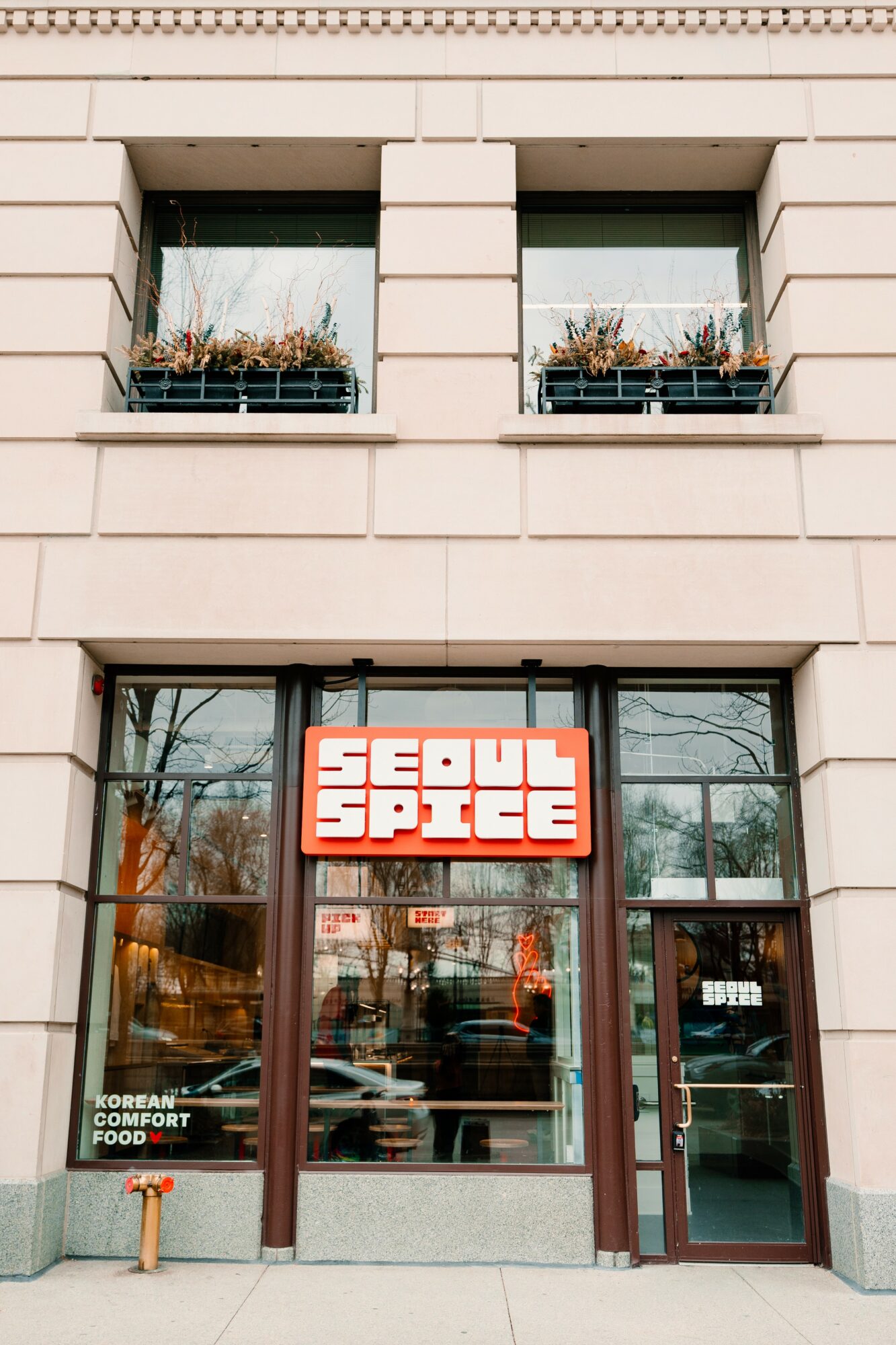 Storefront with a sign reading 'SEDUK SPICE' above glass doors, two windows with plants, and a beige building facade.