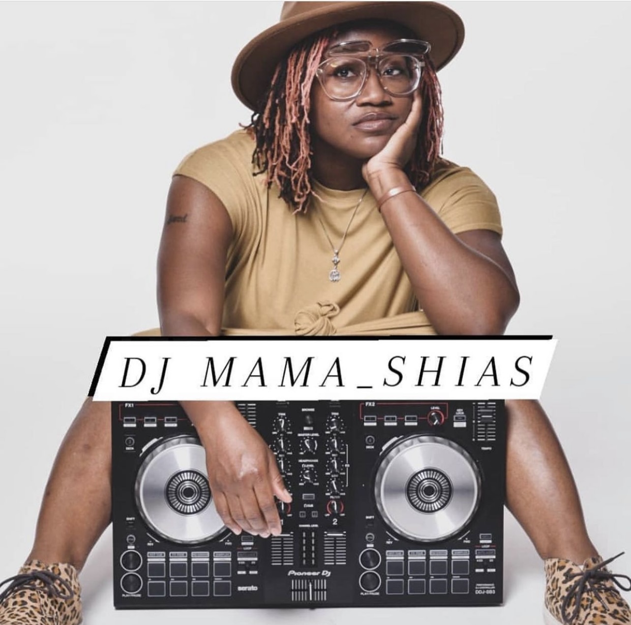 Woman with glasses and hat resting her head on her hand, sitting behind a DJ controller, wearing a yellow shirt.
