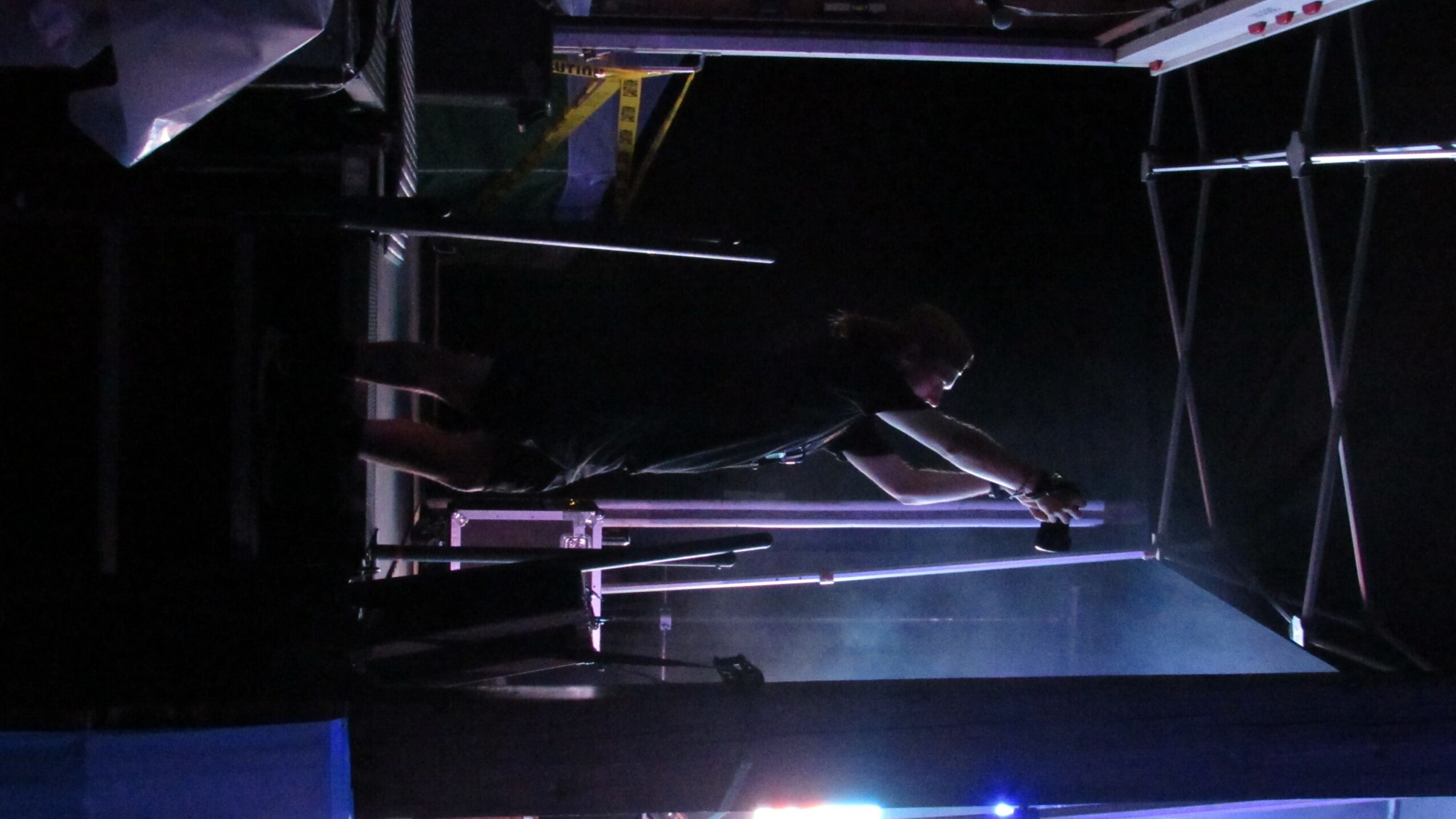 Person reaching out with arm extended in a dark, industrial setting with metal structures and lighting.