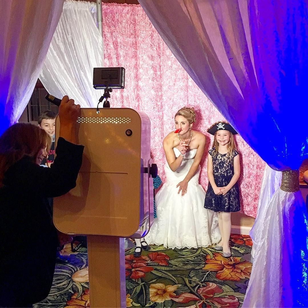 Two young girls and a woman in a dress pose for a photo behind curtains, with a photographer and camera visible.
