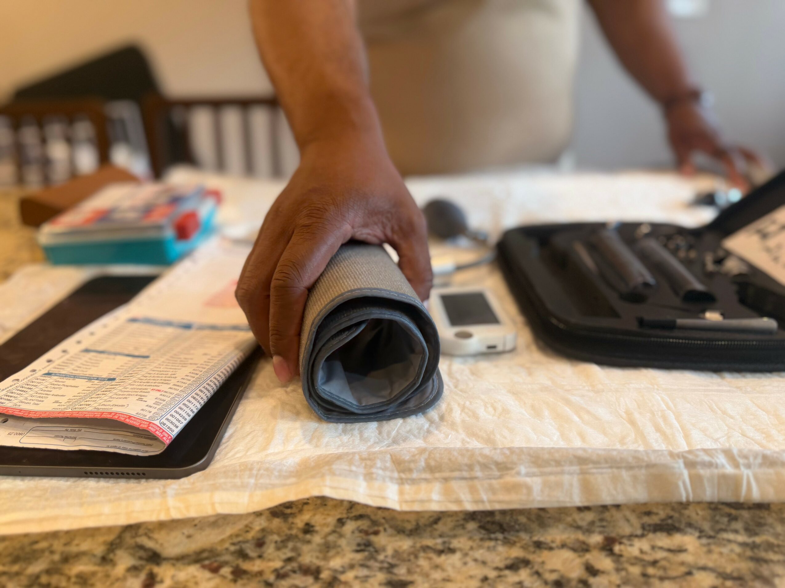 Person's hand holding a rolled-up gray mat on a table with various items, including a notebook, remote, and black case.