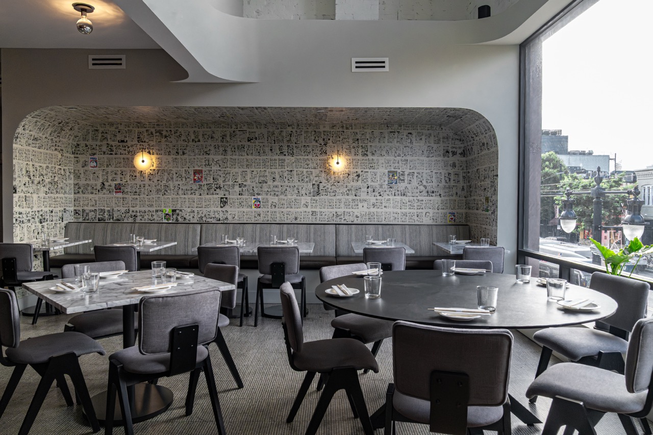 Dining area with tables, chairs, and a large window overlooking an outdoor scene, wall with textured pattern, and ceiling lights.