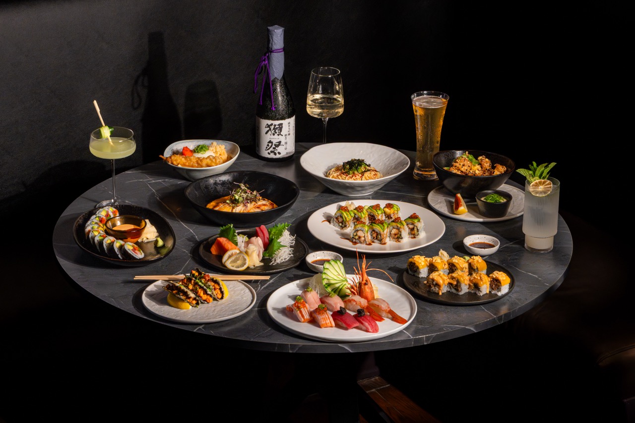 Table with various dishes, drinks, and a bottle of wine, set against a dark background.