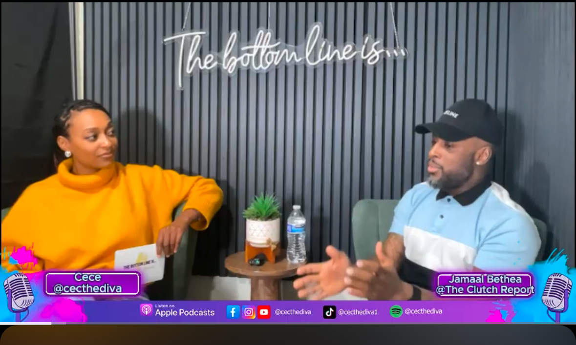 Two people sit at a table with a black background and white text reading 'The bottom line is...'. One wears a yellow sweater, the other a black cap and light blue shirt.