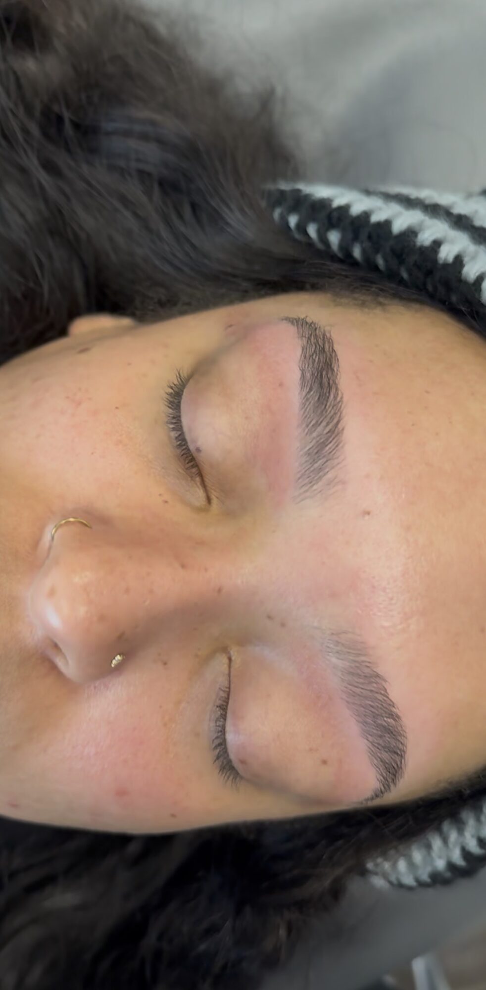 Close-up of a person's face with closed eyes, showing eyebrows and nose, lying down with a patterned fabric nearby.
