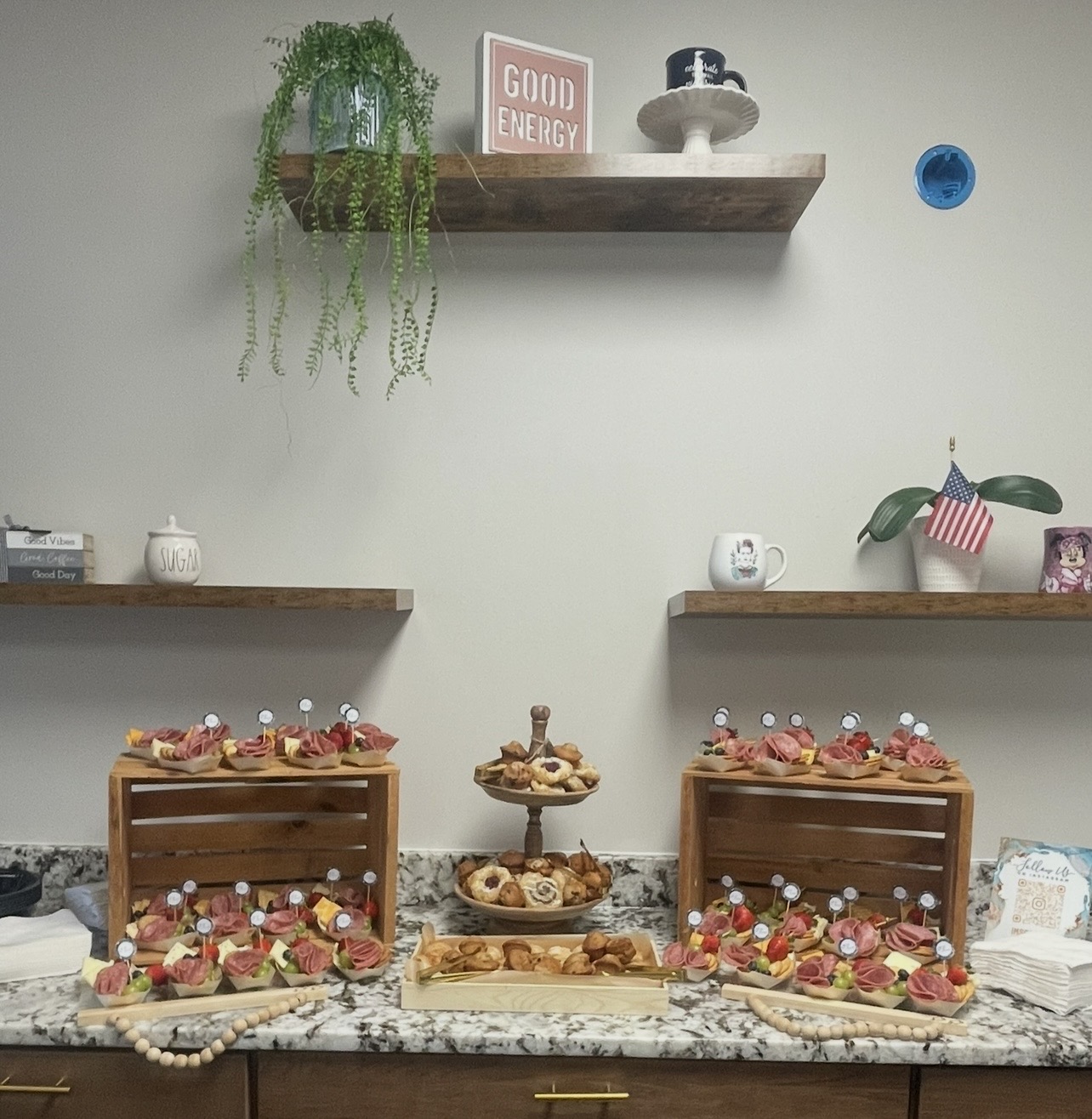 Display of desserts on a marble countertop with two wooden crates filled with pastries, and shelves with decorative items above.