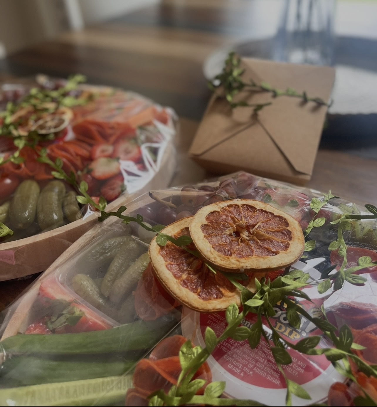 Close-up of packaged dried citrus slices and fresh vegetables on a table with a wrapped gift and a bowl in the background.