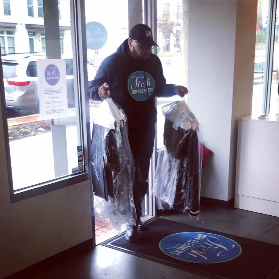 Person holding two plastic bags with clothing inside, standing near glass door inside store, wearing a cap and dark clothing.