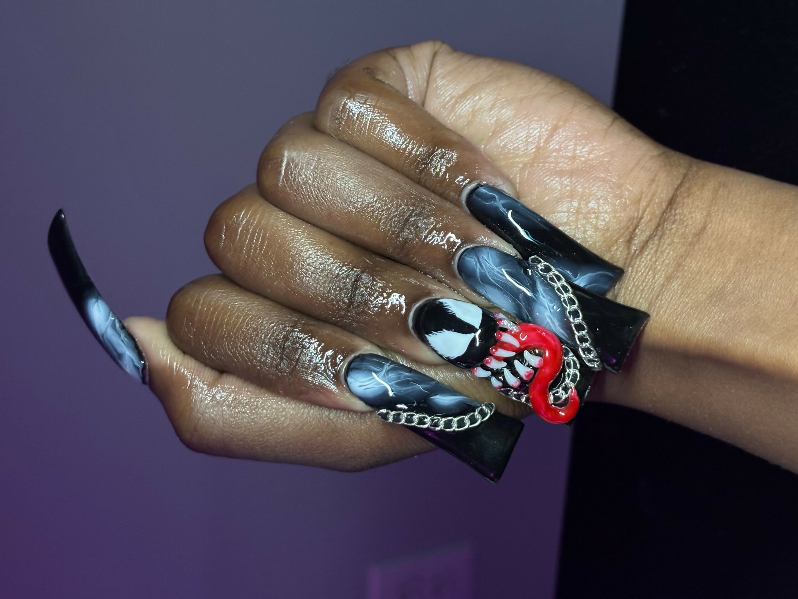 Close-up of hands with black and white nail art, red and white chain design, and shiny skin, against a dark background.