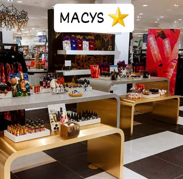 Display of cosmetics and beauty products in a store with tables and shelves, Macy's sign with star, bright lighting.