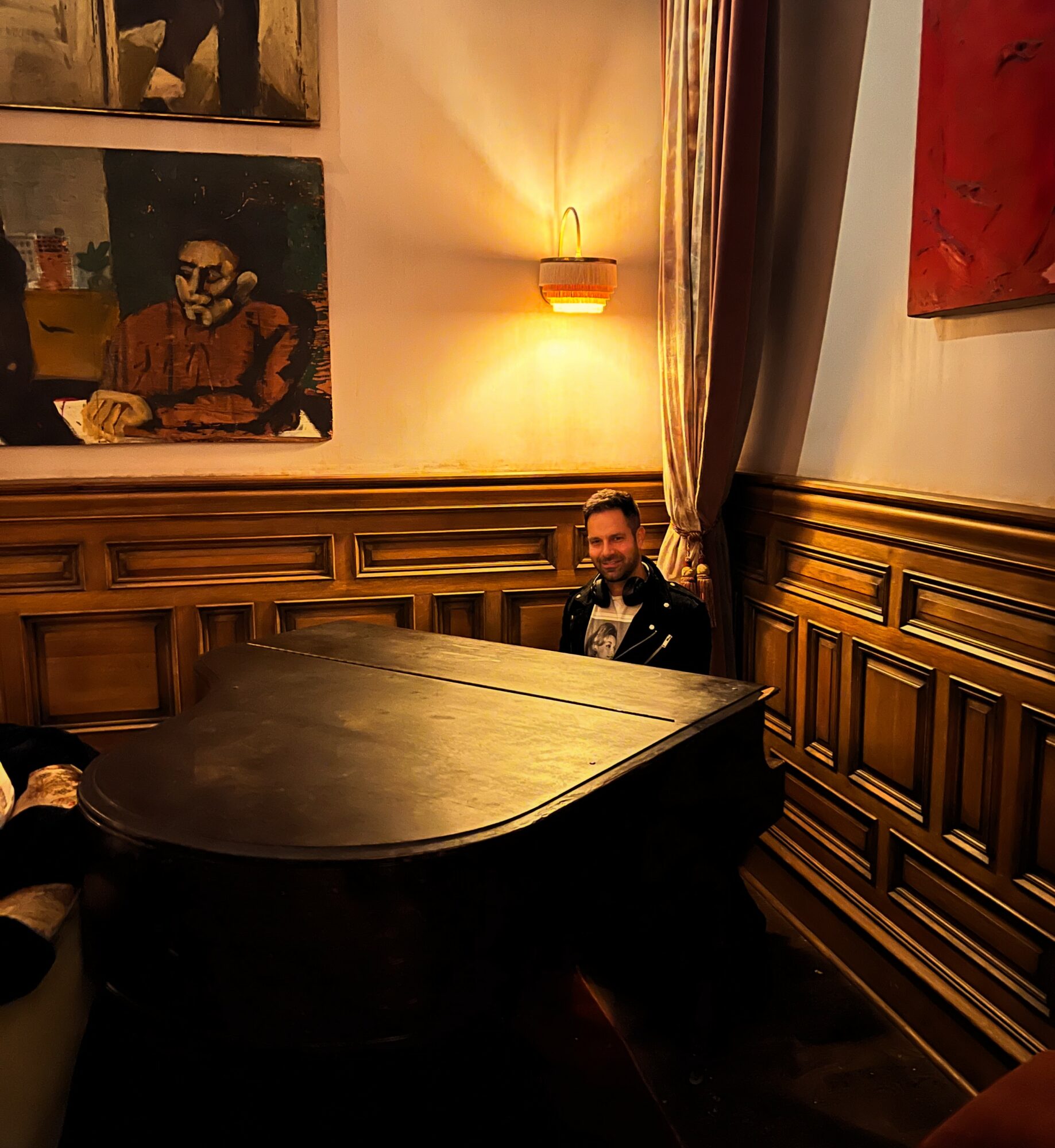 Person sitting at a grand piano in a room with wooden paneling and artwork on the walls.