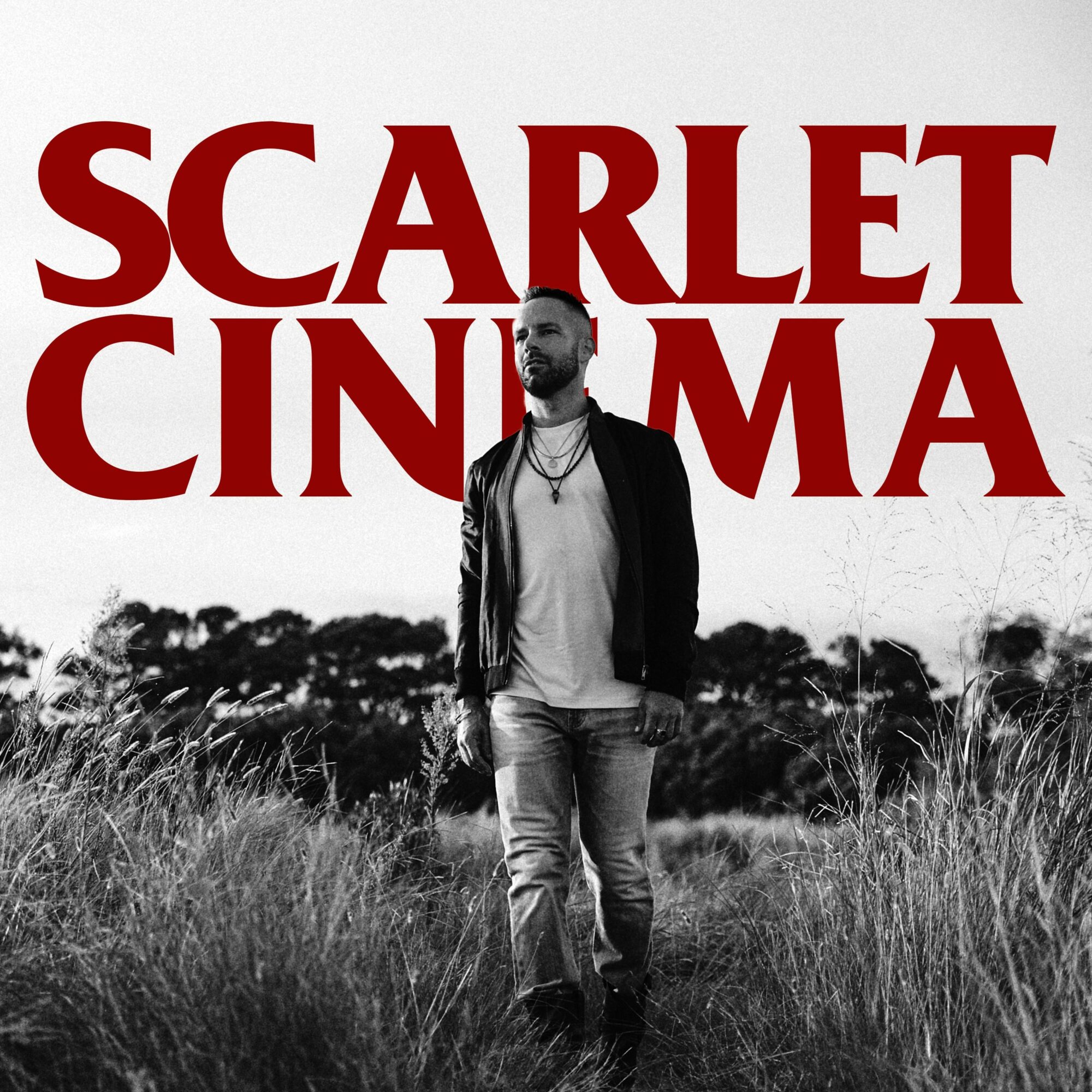 Person standing outdoors in a field with large red text reading 'SCARLET CINEMA' above, black and white background, color text.