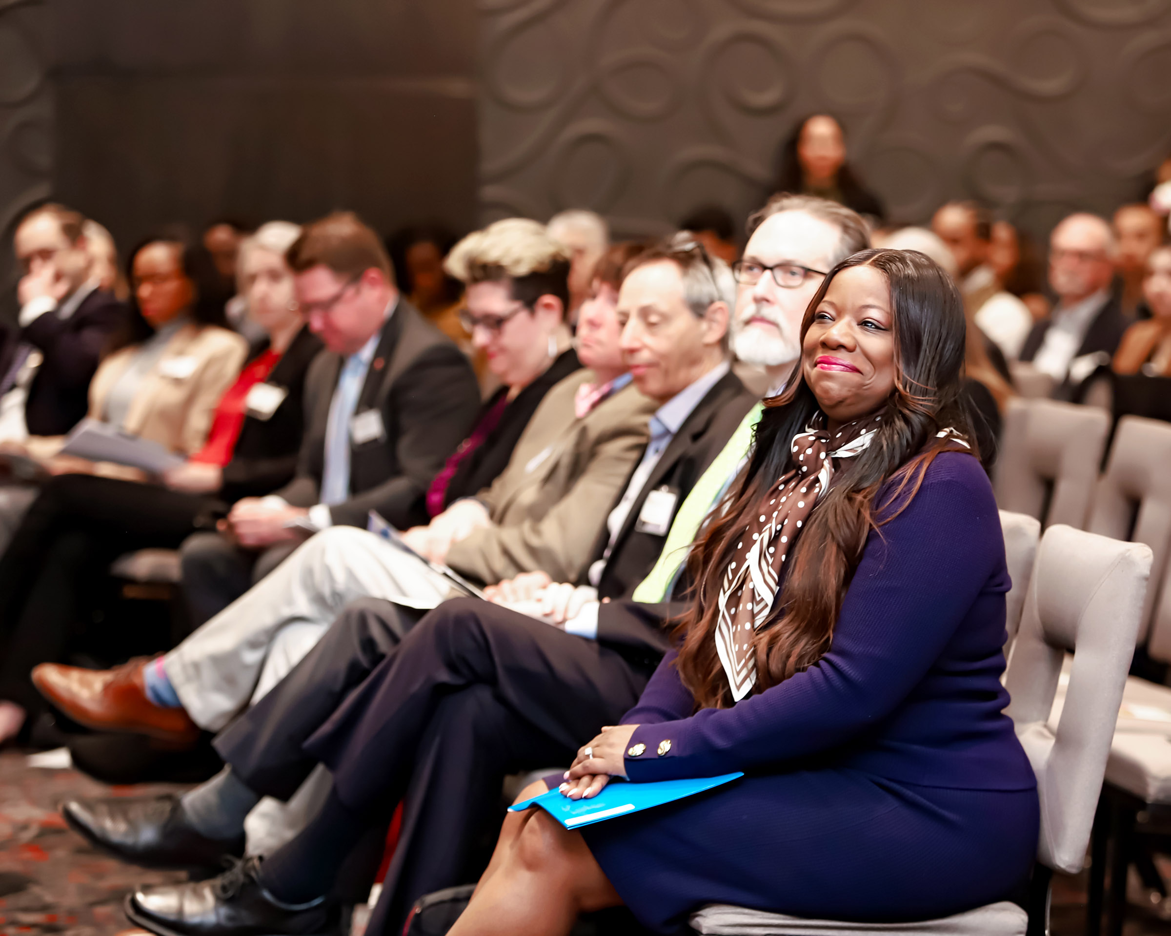 Group of people seated in an auditorium, some smiling, attending an event or conference.