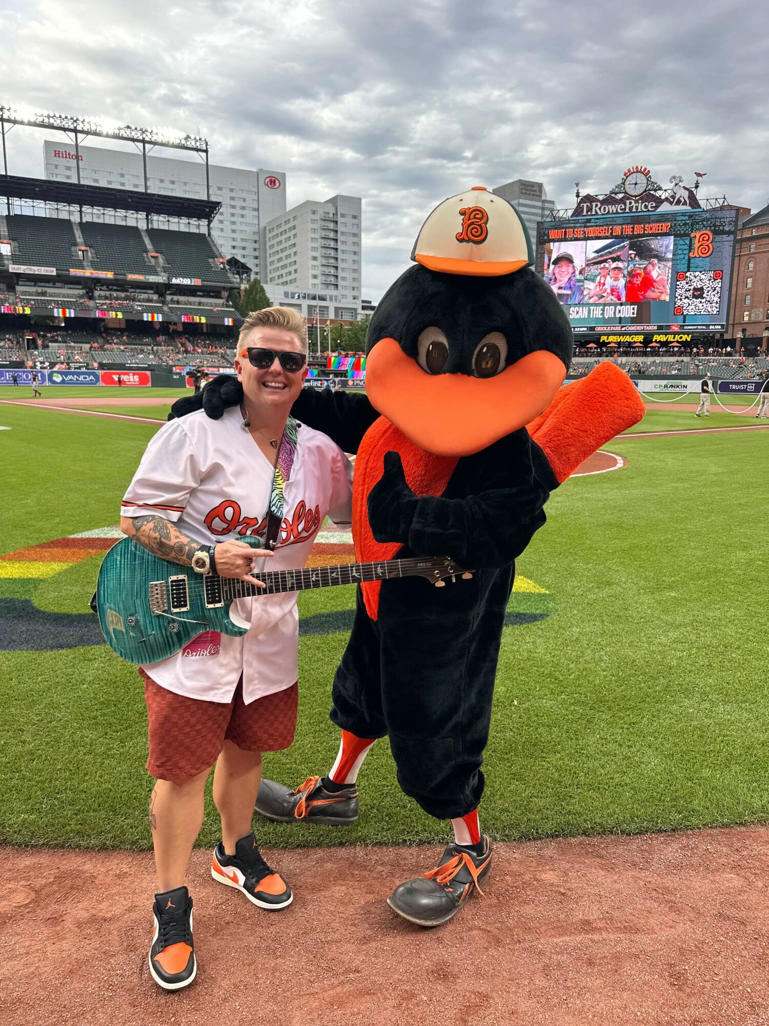 Two people, one in a baseball uniform and the other in a mascot costume, standing on a baseball field.