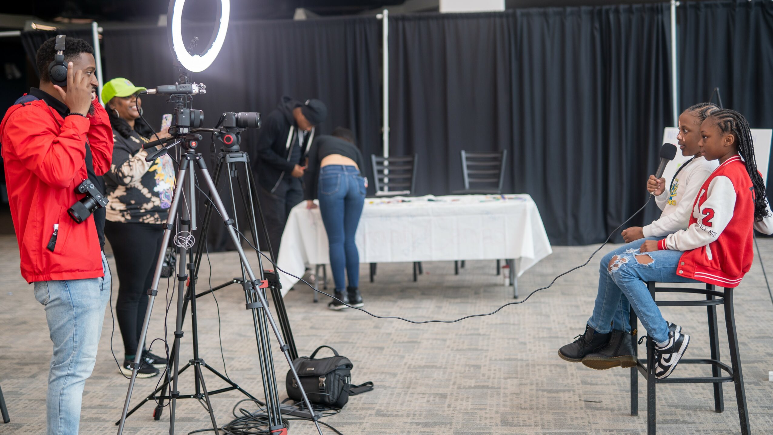 Person being interviewed with a microphone, camera crew filming, and a person adjusting equipment in a studio setting.