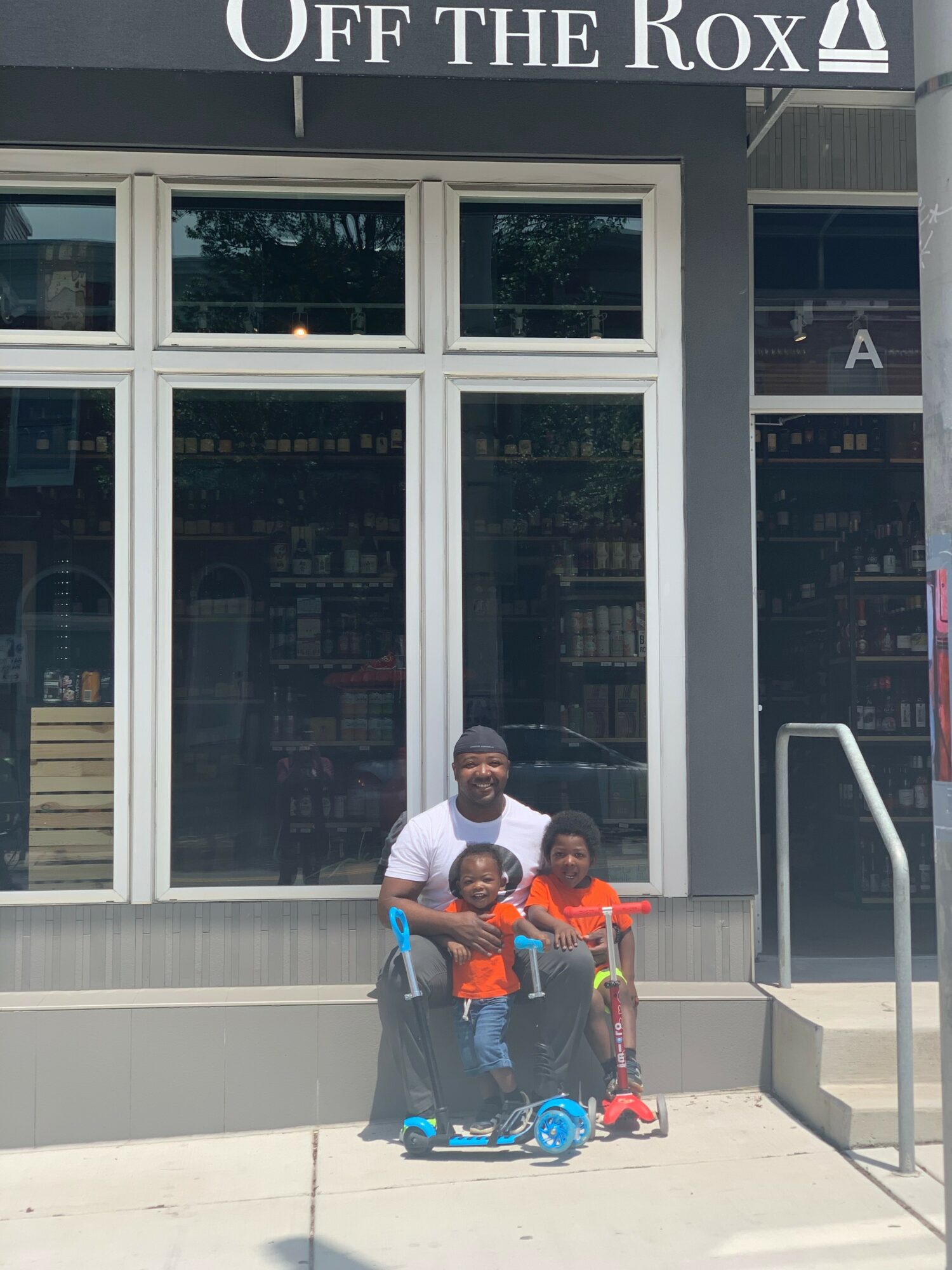 Three children stand outside a store with large windows and a sign reading 'Off the Rox'.