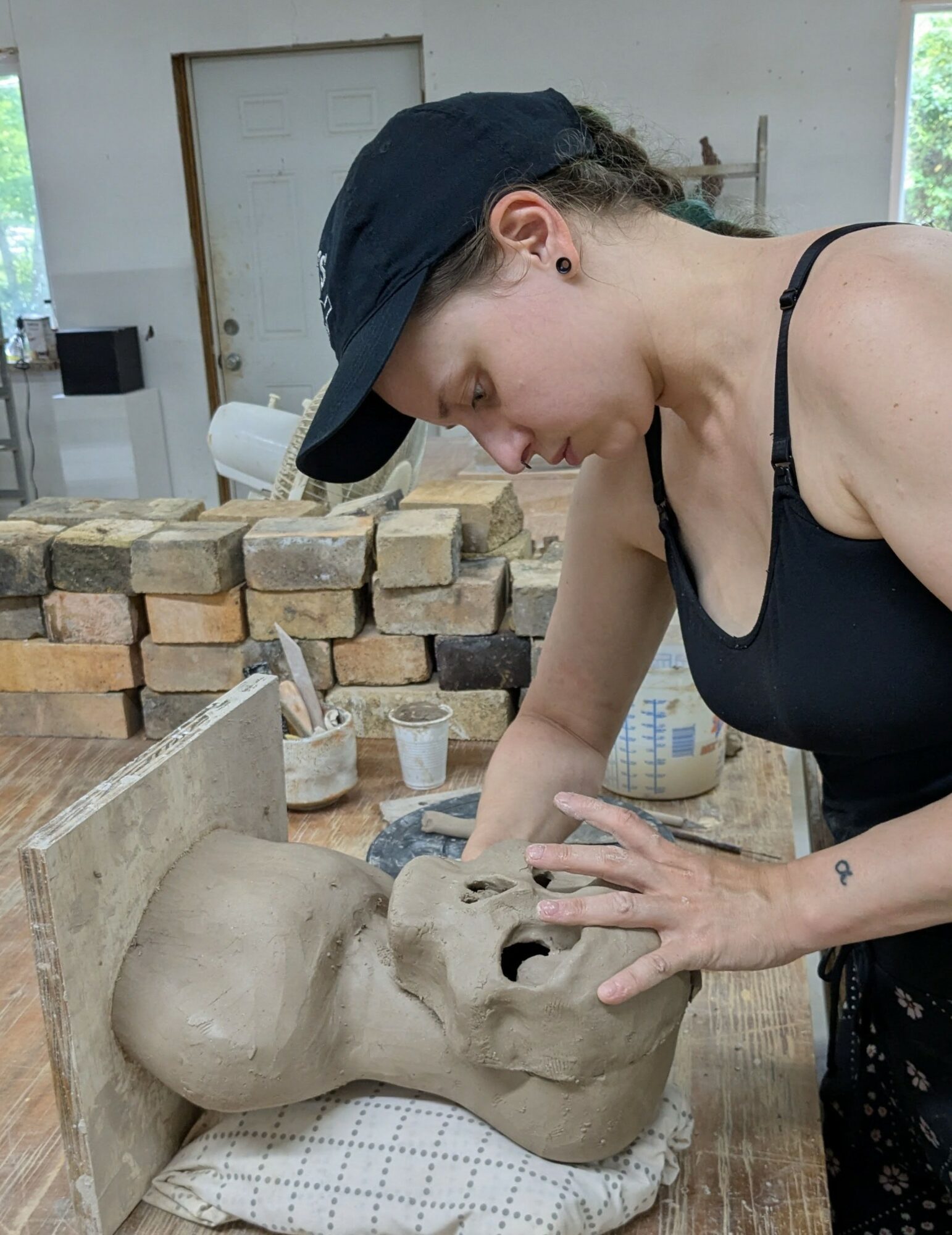Person working on a large sculpture of a face in a workshop with brick walls and tools.