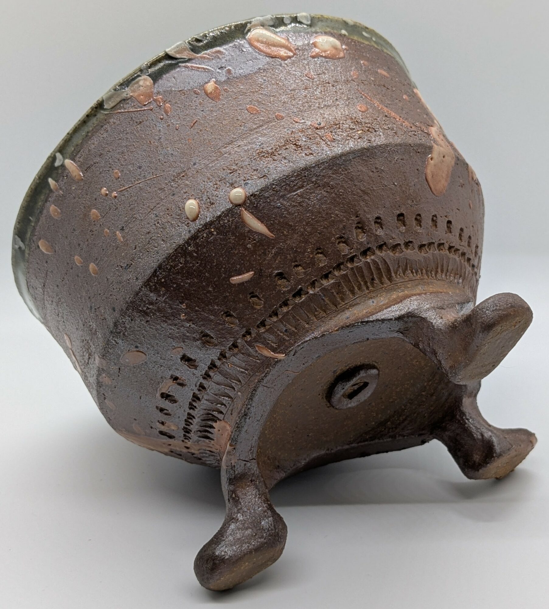 Upside-down metal pot with decorative legs and pinkish residue on surface, on a plain background.