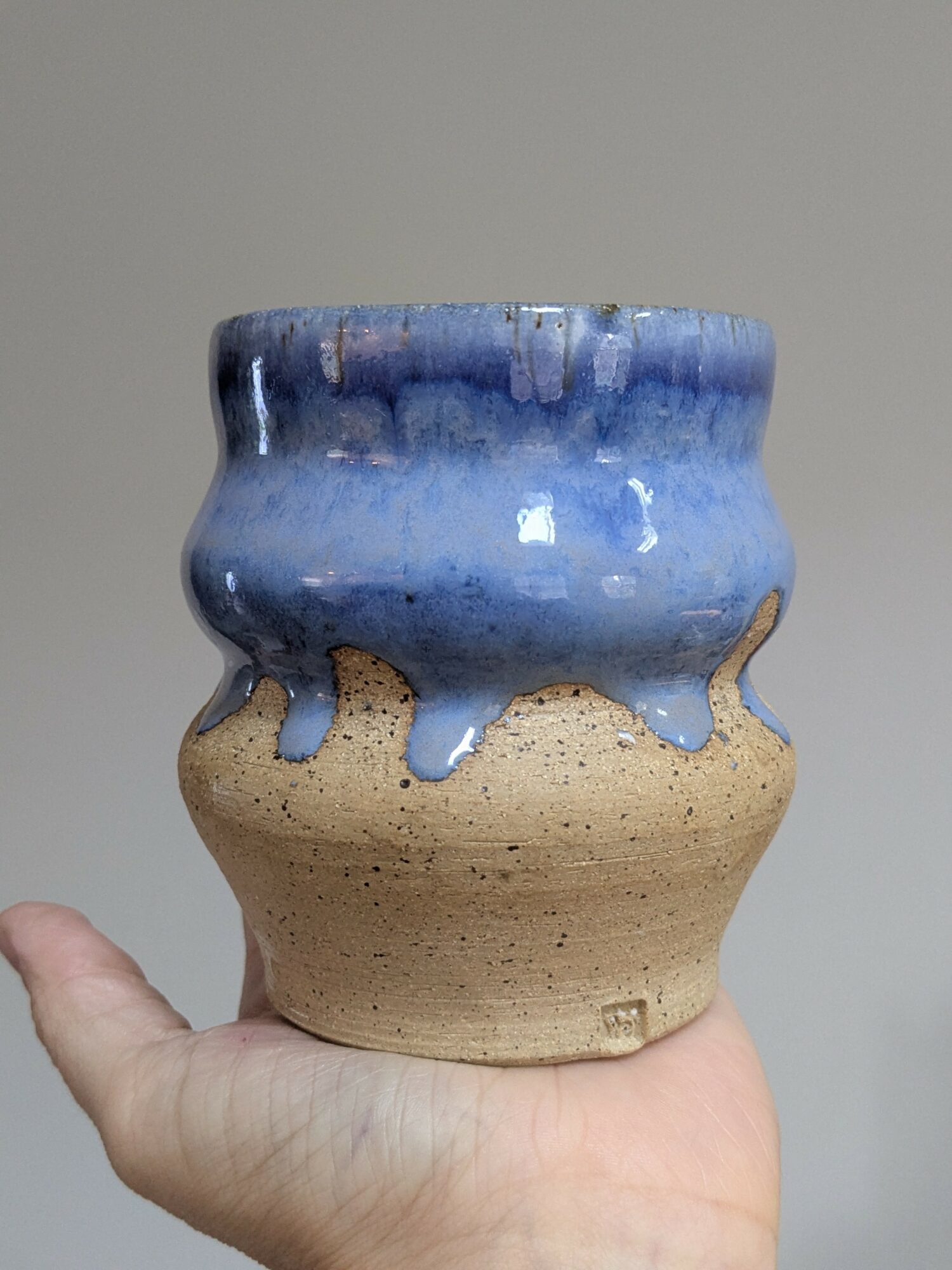 Hand holding a ceramic pot with blue glaze dripping over a beige base.