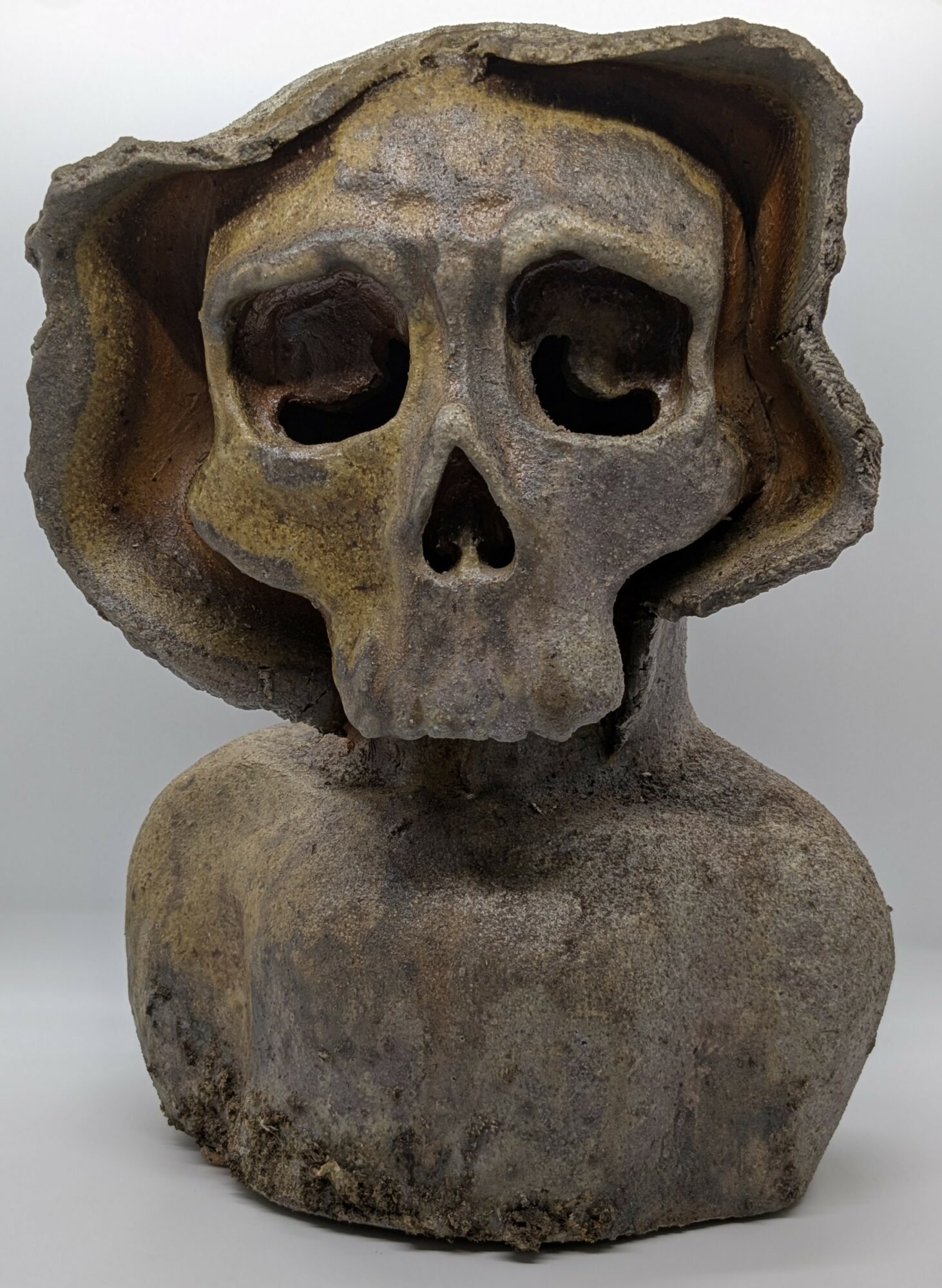 Stone sculpture of a skull with hollow eye sockets and a small nose opening, mounted on a rounded base.