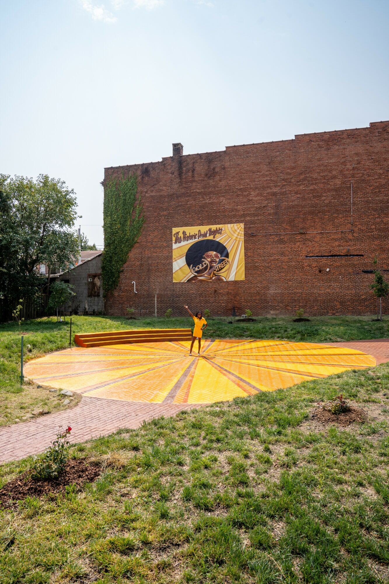 Colorful circular art installation on grass with a brick wall and mural in background.