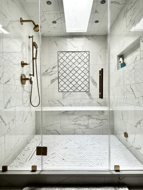 Modern marble shower with glass door, brass fixtures, and a built-in niche, viewed from inside the shower area.