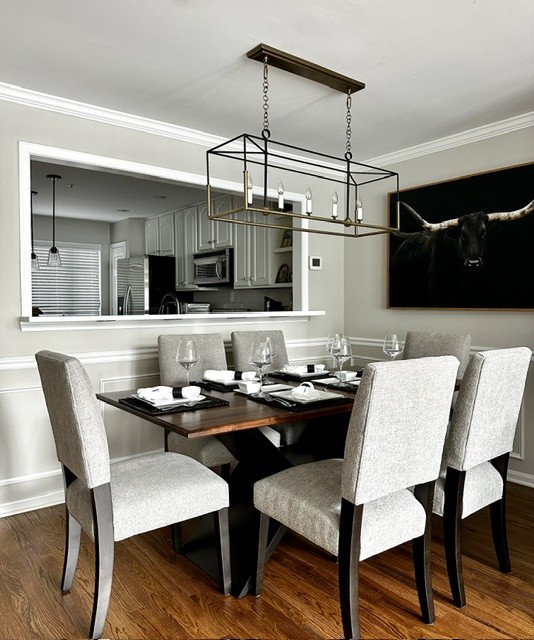 Dining room with six upholstered chairs around a dark wooden table, modern chandelier, and a large painting of a bull on the wall.