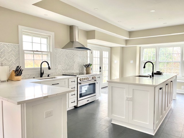 Bright kitchen with white cabinets, island, stainless steel stove, and large windows, sunlight streaming in.