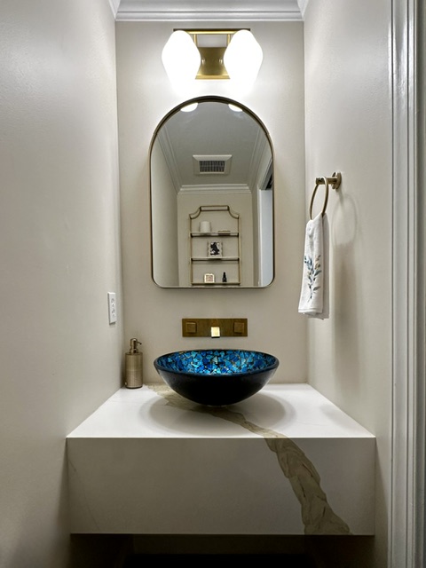 Bathroom vanity with a blue vessel sink, mirror, towel, and wall-mounted light fixture, with a marble streak on the counter.