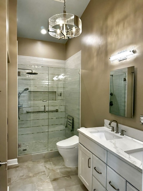 Bathroom with shower, toilet, and vanity with mirror, beige walls, and tiled floor.